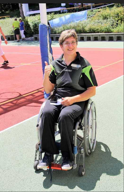 Heike lachend mit ihrem Blasrohr im Rollstuhl